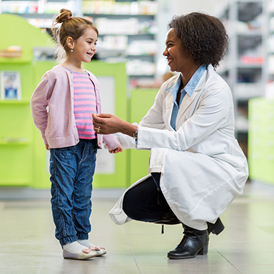 African American pharmacist talking to little girl in pharmacy.